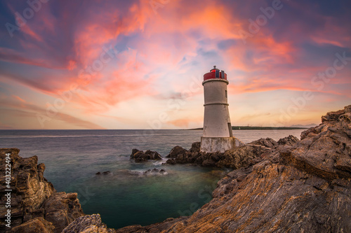 (Selective focus) Stunning view of a rocky coastline with a lighthouse during a dramatic sunset. Sardinia, Italy