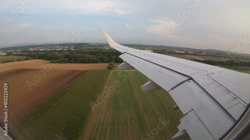 Plane landing. The reduction of a passenger plane over the europian country. Wing in the window. Green field from above on spring or summer sunny day. Blue sky with light clouds.