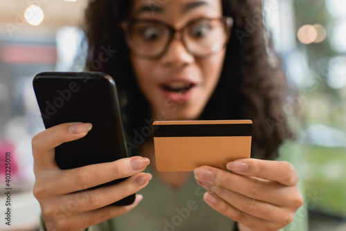 smartphone and credit card in hands of amazed african american woman on blurred background