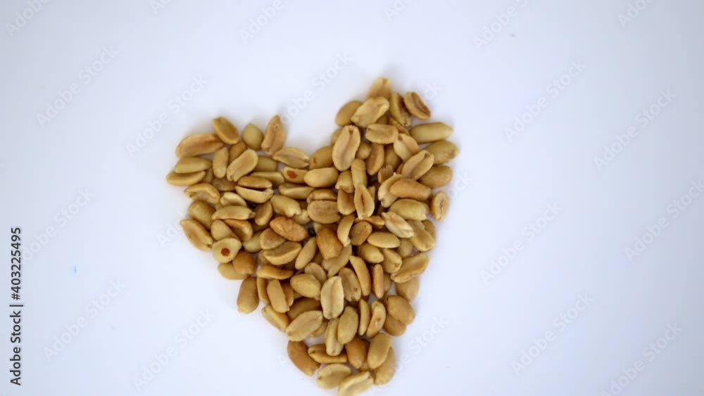 Small pile of peanuts in a heart shape on a white table Small pile of peanuts in a heart shape on a white table