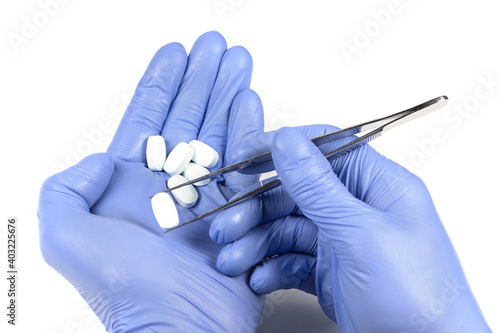 Pharmacology and Medical theme: doctor's hand in a white glove holding tweezers with white pill capsule isolated on white background in studio.