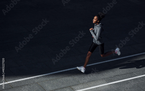 Fast runner. Young african american woman in sportive clothes have workout outdoors at daytime