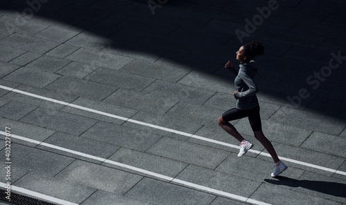 Fast runner. Young african american woman in sportive clothes have workout outdoors at daytime