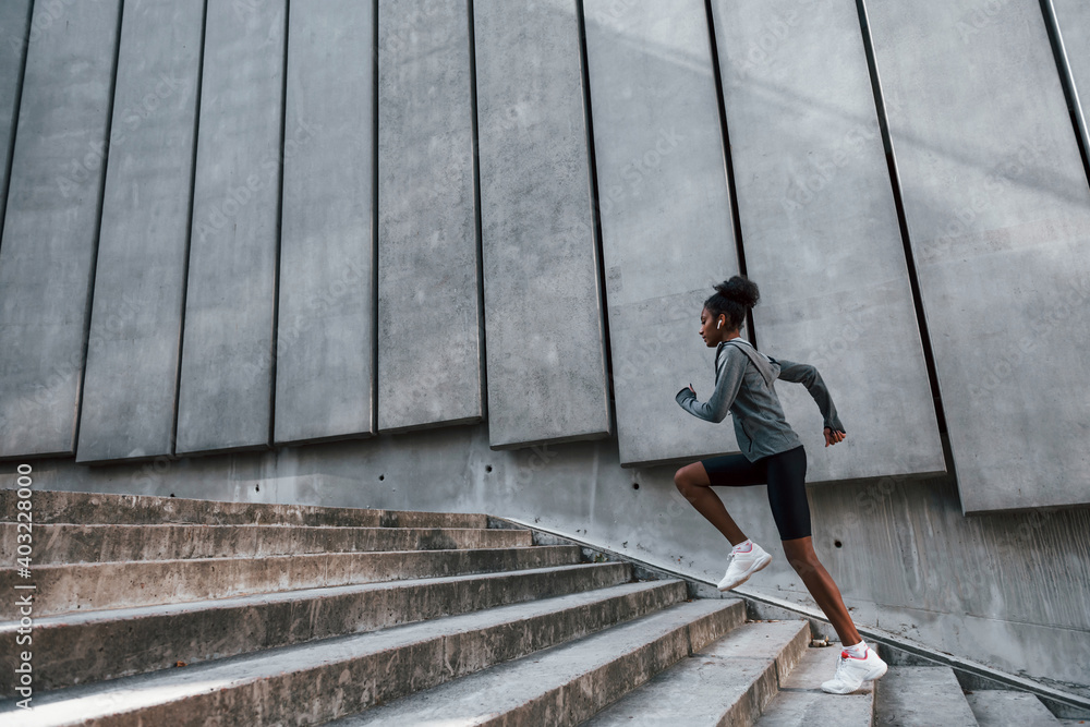 Fast runner. Young african american woman in sportive clothes have workout outdoors at daytime Fast runner. Young african american woman in sportive clothes have workout outdoors at daytime