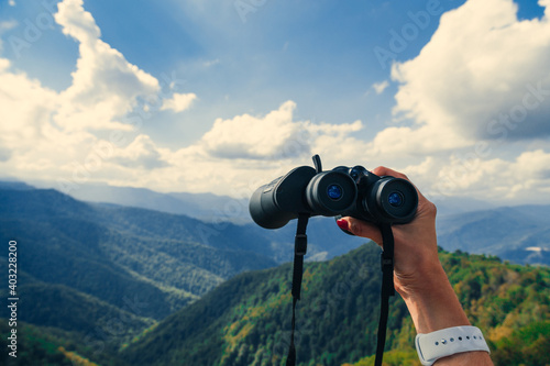 Hands holding binoculars on mountains forest nature background, looking through binoculars, travel, search and search concept. © Nana_studio