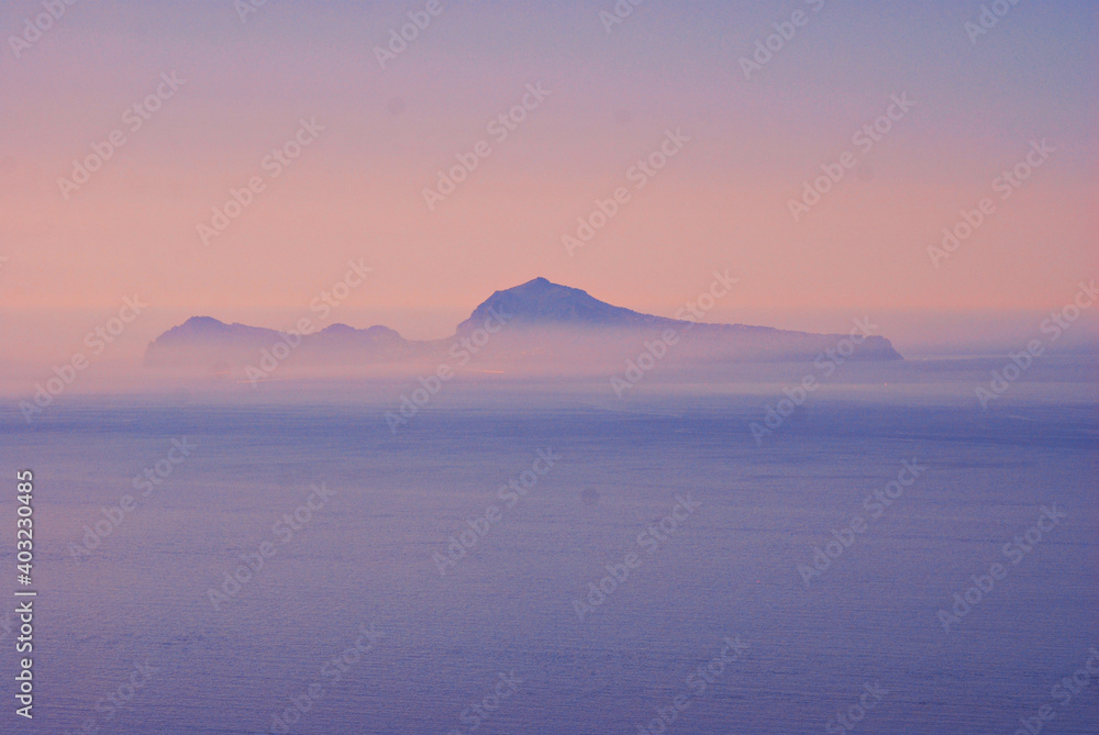 The Capri Island view from the Napoli Gulf in the lightblue evenings fog in south Italy region