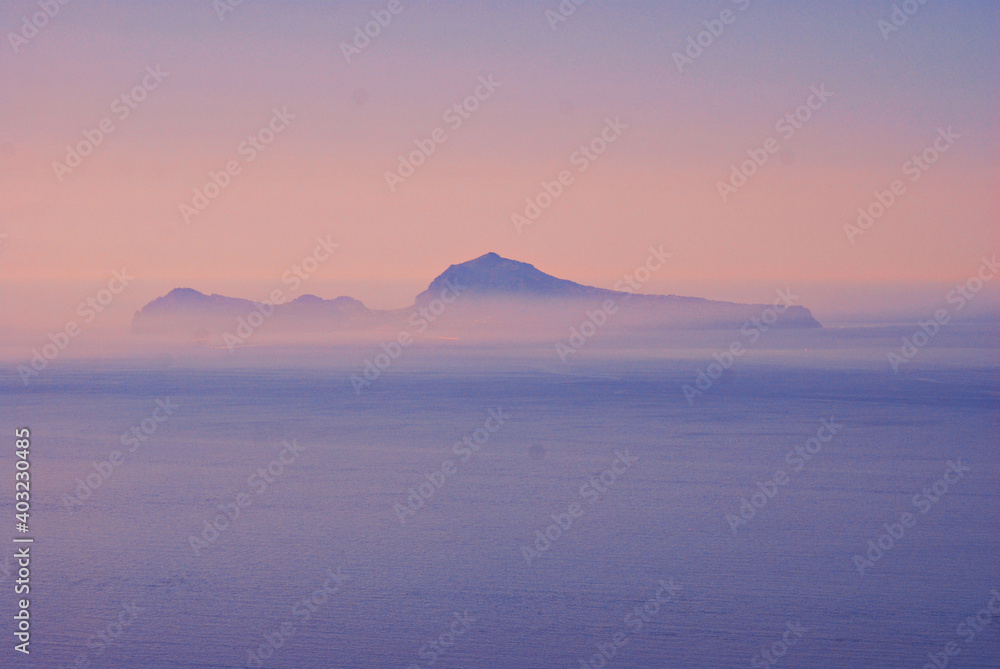 The Capri Island view from the Napoli Gulf in the lightblue evenings fog in south Italy region The Capri Island view from the Napoli Gulf in the lightblue evenings fog in south Italy region