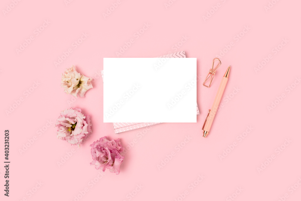 Empty paper card mockup, stationery and flowers on a pink pastel background. Feminine workspace with copyspace. Springtime monochrome concept.