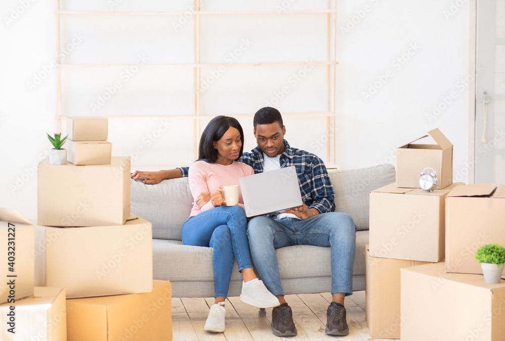 Cheerful black couple using laptop to plan design of their new apartment on moving day Cheerful black couple using laptop to plan design of their new apartment on moving day