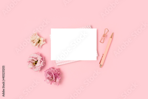Empty paper card mockup, stationery and flowers on a pink pastel background. Feminine workspace with copyspace. Springtime monochrome concept.