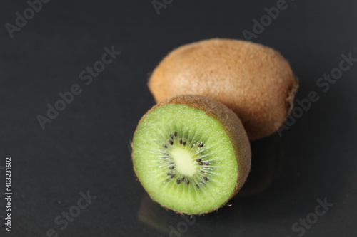 Whole and half fruit kiwi berries lie on a black background with a copyspace