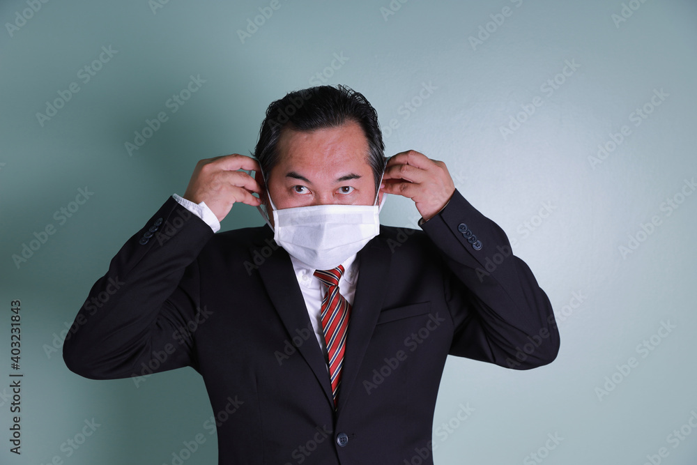 Portrait Asian businessman wears a black suit looking at the camera. Two hands holding medical masks are wearing to prevent coronavirus. Portrait Asian businessman wears a black suit looking at the camera. Two hands holding medical masks are wearing to prevent coronavirus.
