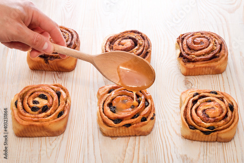 Freshly baked sweet bun with raisins and cinnamon on wooden table. Glazing a Cinnabons won. Homemade traditional bakery, baking bread and sweets concept. photo