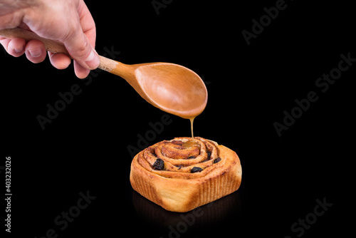 Freshly baked sweet bun with raisins, cinnamon and sweet glaze isolated on black background. Homemade traditional bakery, baking bread and sweets concept. photo