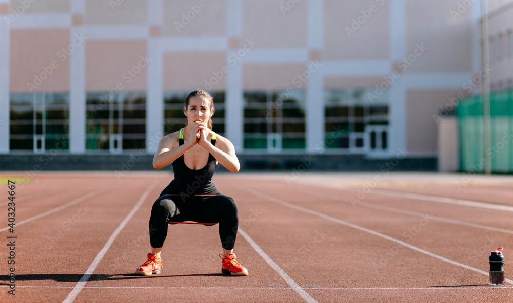 Fototapeta premium Female runner stretching leg muscles in a black sports clothes