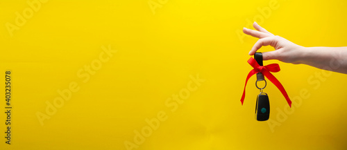 Woman's hand holds car keys. Car keys as a gift on a yellow background
