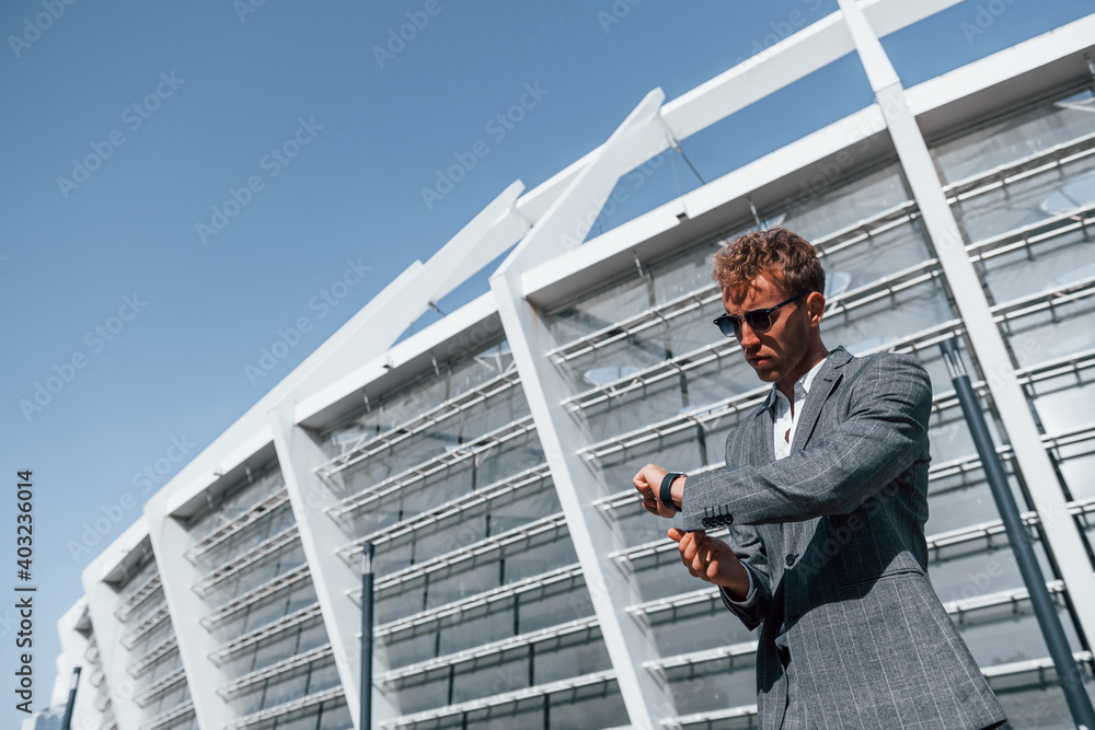 Big stadium behind. Young businessman in grey formal wear is outdoors in the city Big stadium behind. Young businessman in grey formal wear is outdoors in the city