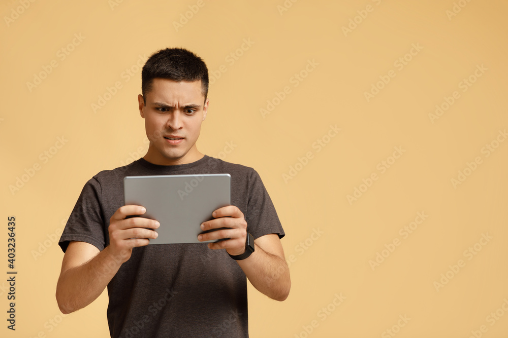 Strange video, shocking information, weird message. Surprised and upset man looks in digital tablet and reads news Strange video, shocking information, weird message. Surprised and upset man looks in digital tablet and reads news