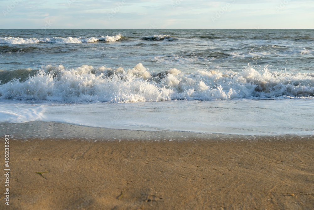 Sandy coast with waves, foam and blue sky