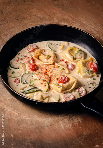 Ravioli in the white sauce with vegetables in pan on the wooden table.