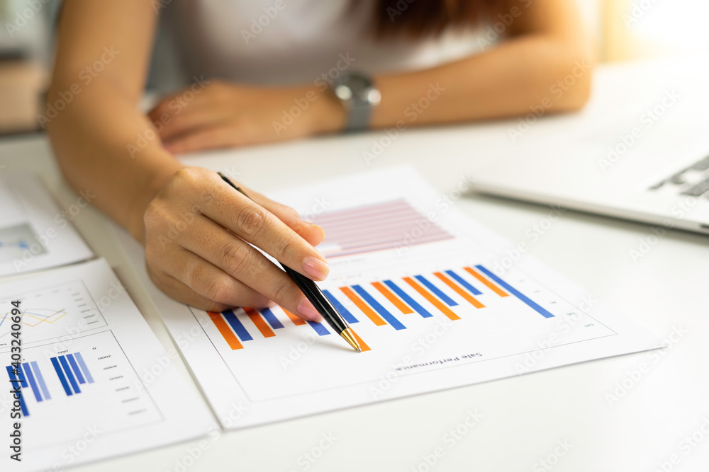 Asian female finance staff is pointing a pen at the report. In the form of a bar graph That represents the highest point of the company's profits to explain to her boss, the business concept, growth a Asian female finance staff is pointing a pen at the report. In the form of a bar graph That represents the highest point of the company's profits to explain to her boss, the business concept, growth a