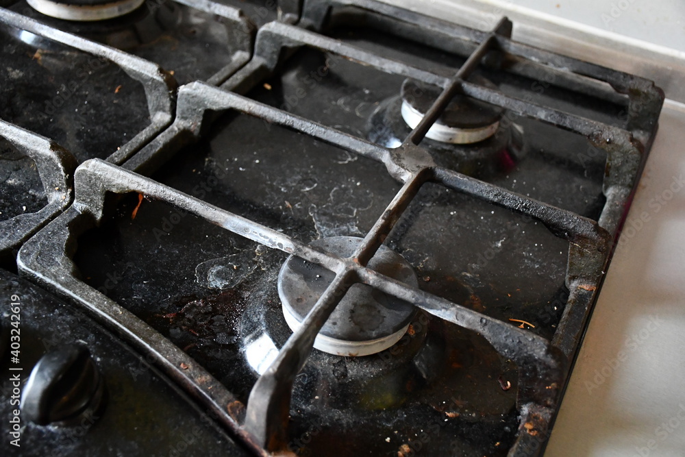 A dirty, stained and dusty black gas stove hob with cast-iron grilles. A dirty, stained and dusty black gas stove hob with cast-iron grilles.