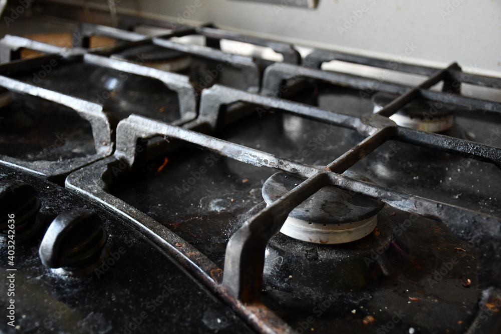 A dirty, stained and dusty black gas stove hob with cast-iron grilles. A dirty, stained and dusty black gas stove hob with cast-iron grilles.