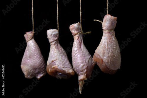 Raw chicken legs on a black background. Chicken legs hang suspended by a thread. Chicken meat.