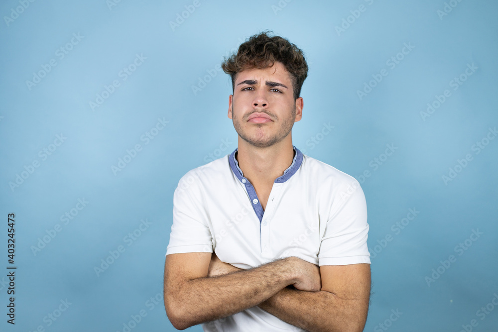 Young handsome man wearing a white t-shirt over blue background thinking looking tired and bored with crossed arms