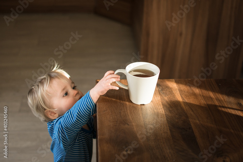 Little child try to grab cup of hot tea on the table. Attention hot content concept.