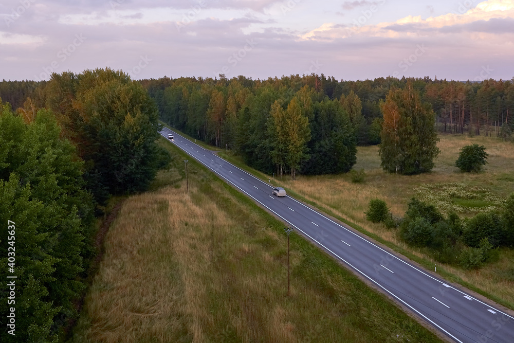 Cars on a rural asphalt road next to forest in summertime
