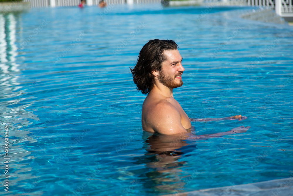 Portrait of a sexy handsome man resting at swimming pool. Summer vacation concept.