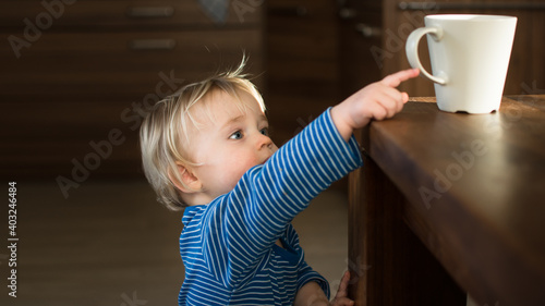 Little child try to grab cup of hot tea on the table. Attention hot content concept.