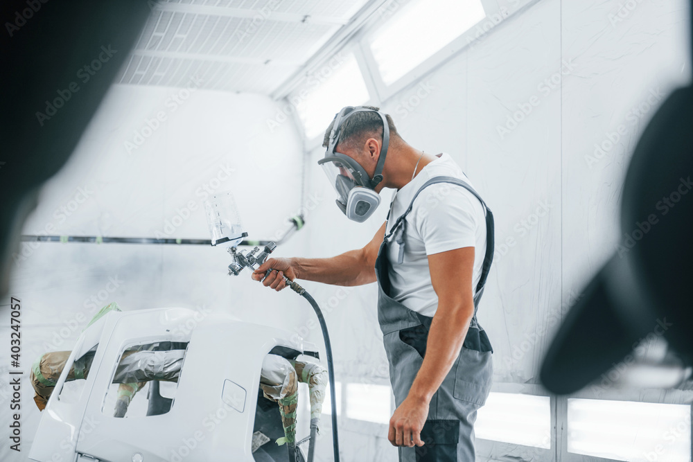Uses painting gun. Caucasian automobile repairman in uniform works in garage Uses painting gun. Caucasian automobile repairman in uniform works in garage
