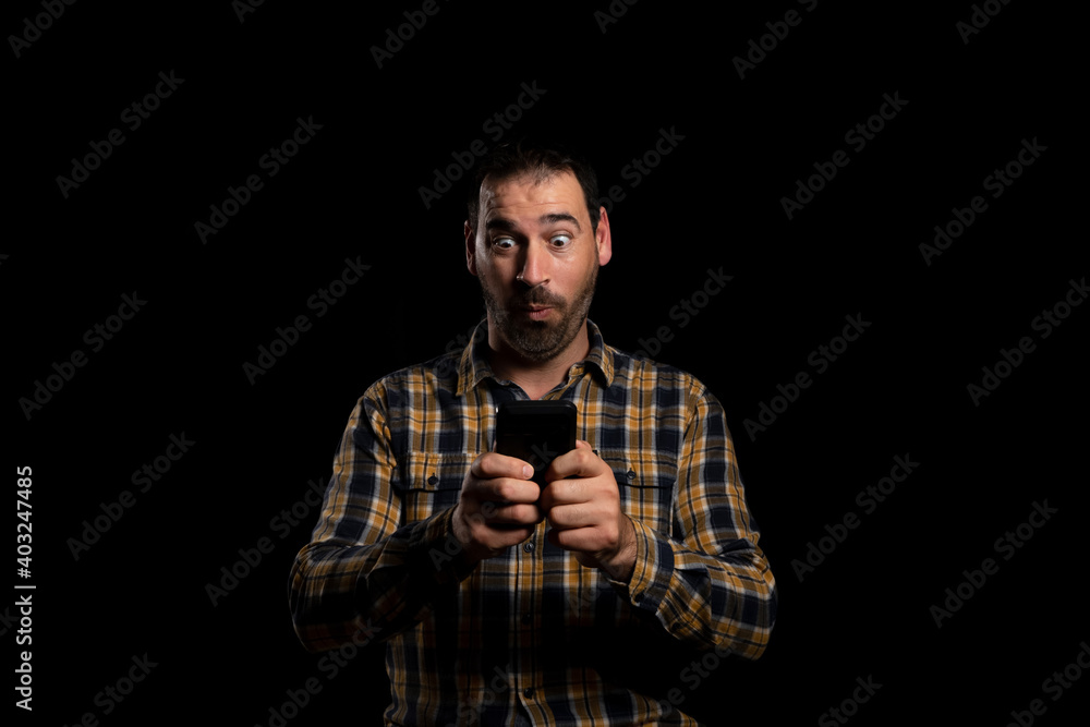 Attractive bearded man in a yellow plaid shirt using mobile isolated on black background Attractive bearded man in a yellow plaid shirt using mobile isolated on black background