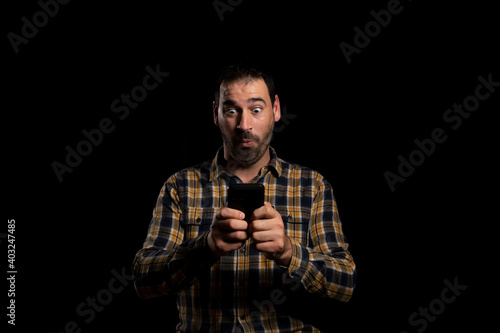 Attractive bearded man in a yellow plaid shirt using mobile isolated on black background