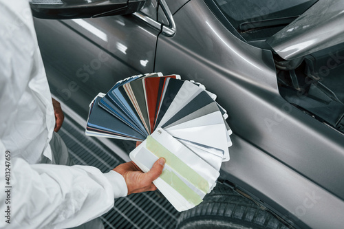 Holds cards with different colors. Caucasian automobile repairman in uniform works in garage