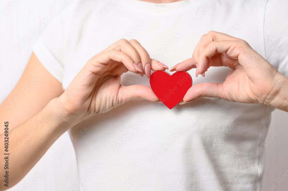 The girl holds a red heart on her chest as a symbol of love and health. Heart disease concept The girl holds a red heart on her chest as a symbol of love and health. Heart disease concept
