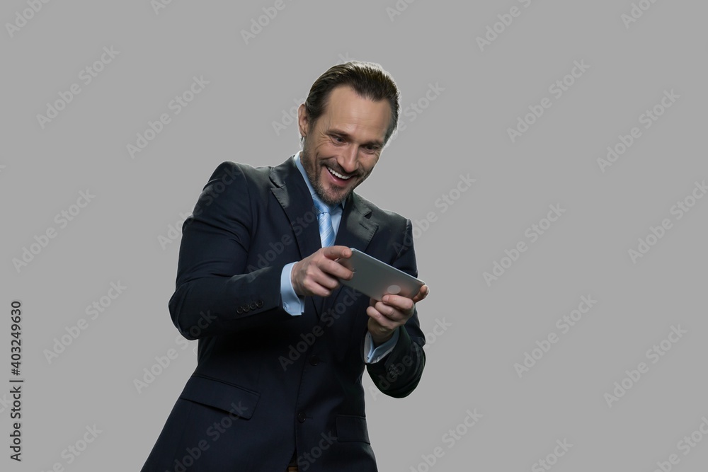 Cheerful businessman playing a video game. Excited manager playing game on smartphone against gray background. Cheerful businessman playing a video game. Excited manager playing game on smartphone against gray background.