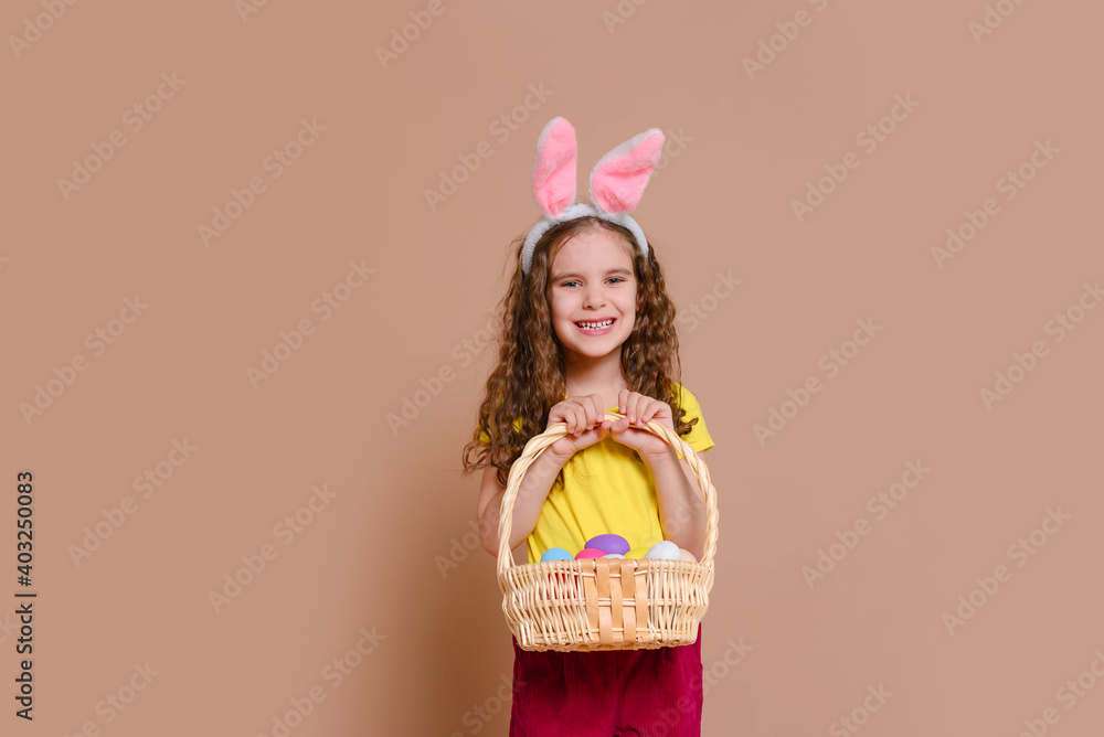  Cute girl child  with Easter bunny ears holds a basket of colored eggs. Happy Easter, holidays, traditions concept.