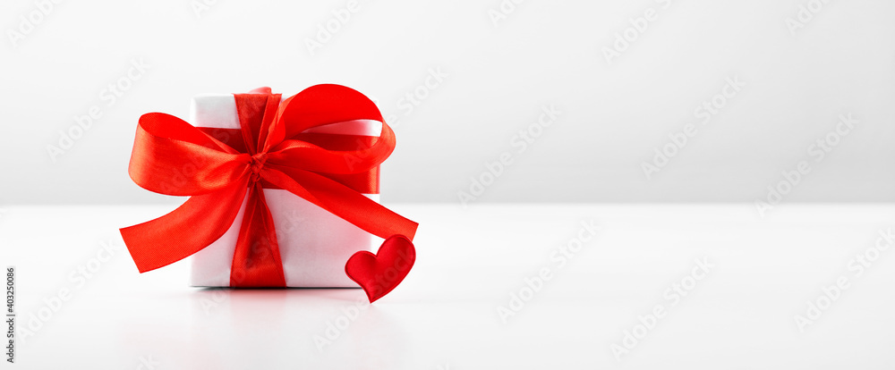 Gift box with red bow ribbon and red paper heart on white table for Valentines day with copyspace. Gift box with red bow ribbon and red paper heart on white table for Valentines day with copyspace.