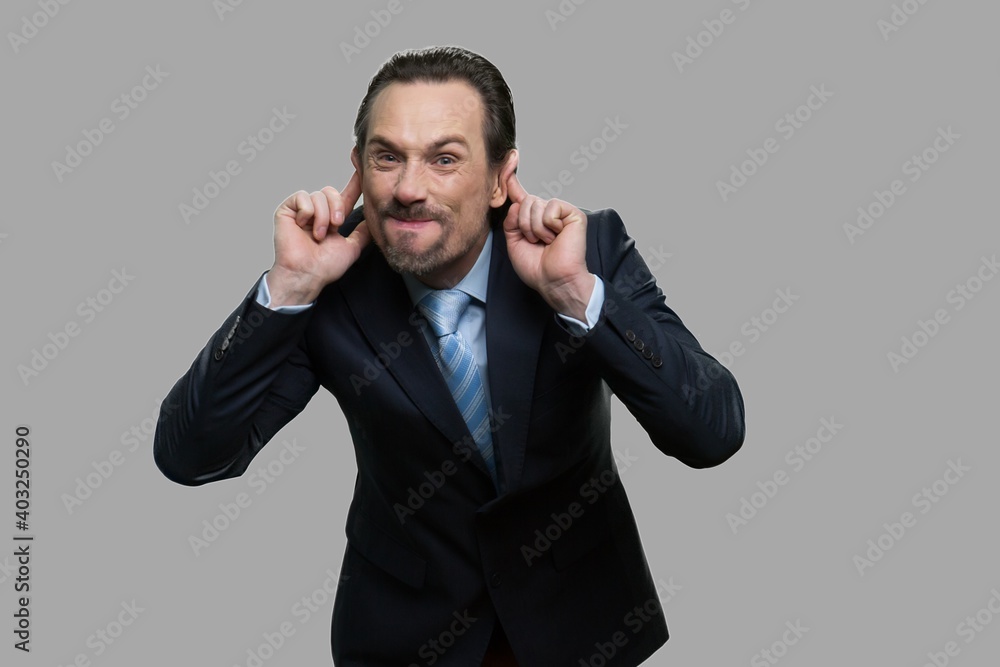 Mature businessman making monkey face. Caucasian man in business suit grimacing and teasing someone on gray background. Mature businessman making monkey face. Caucasian man in business suit grimacing and teasing someone on gray background.