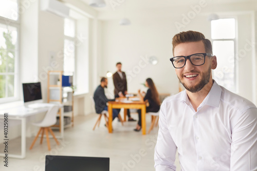 Smiling office worker looking at camera with colleagues having brainstorm at background © Studio Romantic