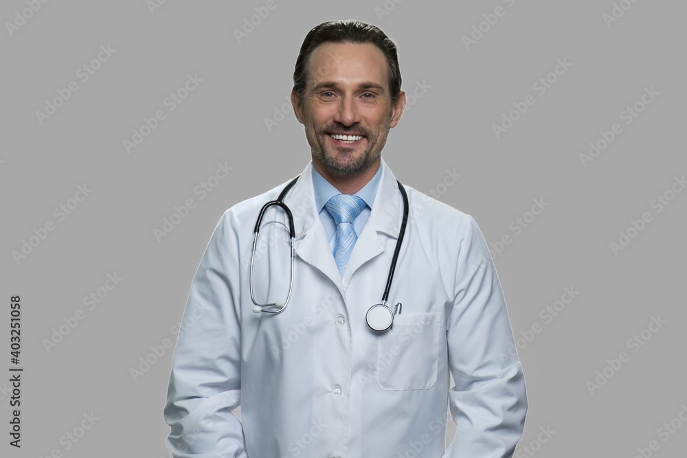 Portrait of smiling male doctor looking at camera. Handsome doctor with stethoscope standing against gray background. Portrait of smiling male doctor looking at camera. Handsome doctor with stethoscope standing against gray background.