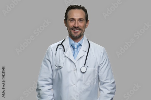 Portrait of smiling male doctor looking at camera. Handsome doctor with stethoscope standing against gray background.