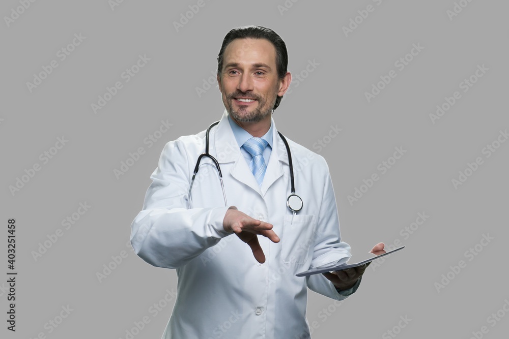Handsome caucasian doctor giving a lecture. Smiling practitioner talking to audience while holding pc tablet against gray background. Handsome caucasian doctor giving a lecture. Smiling practitioner talking to audience while holding pc tablet against gray background.