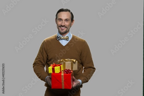 Smiling mature man holding gift boxes. Handsome man with gift boxes on gray background. Space for text.