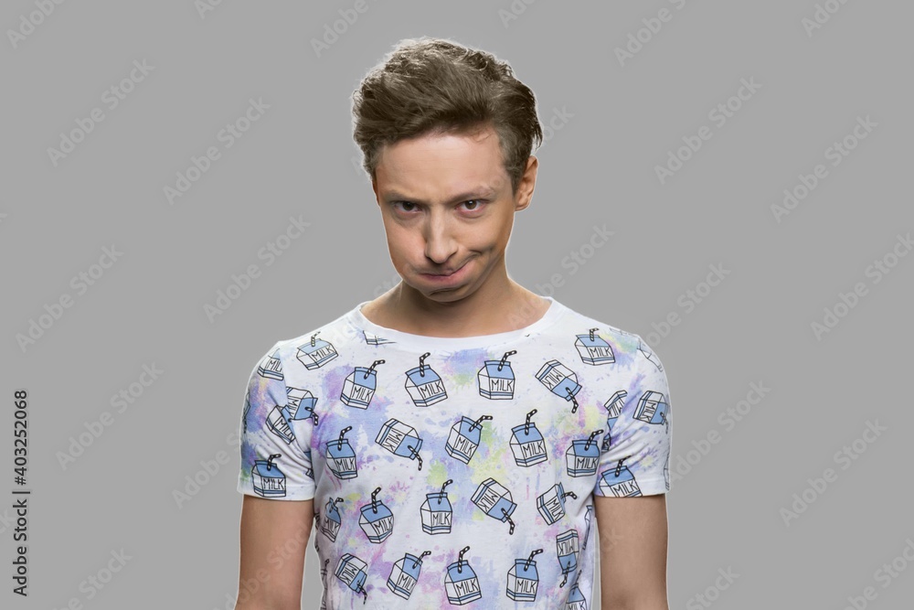 Teenage boy grimacing against gray background. Displeased teen guy making silly face. Upset kid looking at camera. Teenage boy grimacing against gray background. Displeased teen guy making silly face. Upset kid looking at camera.