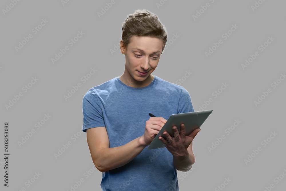 Teenage boy making a note on digital tablet. Handsome teen guy working on tablet pc against gray background. Teenage boy making a note on digital tablet. Handsome teen guy working on tablet pc against gray background.