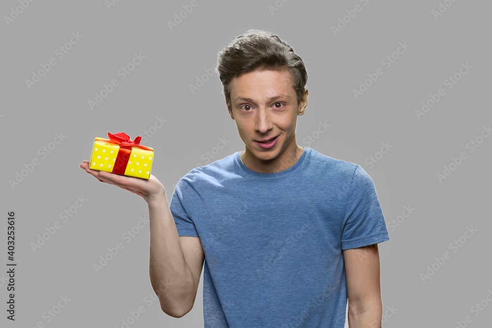 Caucasian teen boy holding small yellow gift box. Teenage guy holding present box on his palm against gray background. Caucasian teen boy holding small yellow gift box. Teenage guy holding present box on his palm against gray background.